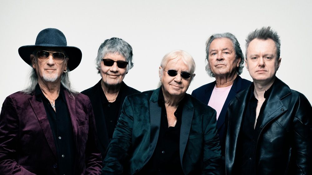 Bandfoto von Deep Purple vor einem weißen Hintergrund. Alle tragen dunkle Kleidung, drei von ihnen haben eine Sonnenbrille auf. 