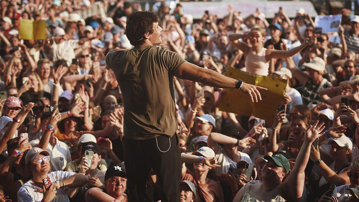 Es ist ein Bild von einem Live-Open-Air-Konzert, fotografiert mit Blick von der Bühne aufs Publikum. Wincent Weiss ist von hinten zu sehen. 