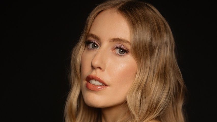 Pressefoto von LEA. Sie steht seitlich, hat den Kopf zur Kamera gedreht. Sie trägt ein schulterfreies Top, ihre langen, blonden Haare sind offen. 