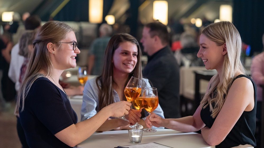Drei junge Frauen unterhalten sich und stoßen im BACKSTAGE CLUB an.