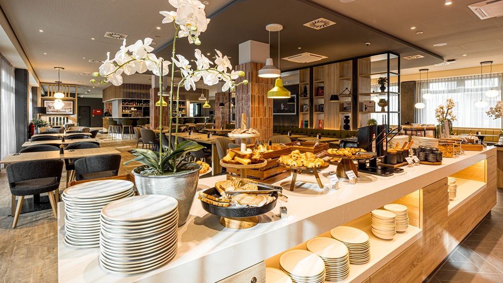 Bild des Frühstücksbereichs des Hotels. Im Vordergrund ist das Buffet, im Hintergrund der Essbereich. 