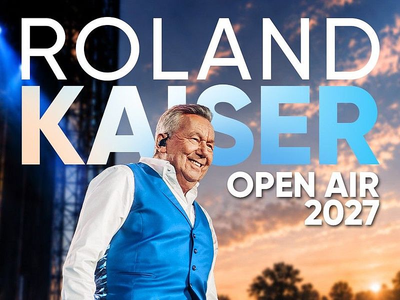Grafik der Tour von Roland Kaiser mit dem Schriftzug Roland Kaiser Open Air 2027. Roland Kaiser steht auf der Bühne, er trägt eine blaue Weste und ein weisses Hemd. Ein stimmungsvoller Abendhimmel mit untergehender Sonne ist zu sehen. 
