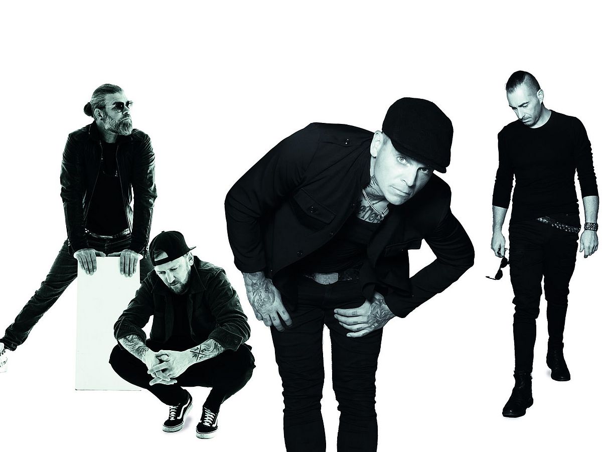 Die vier Bandmitglieder stehen in einem Dreieck, einer hockt. Alle tragen schwarze Kleidung und stehen vor einem weißen Hintergrund. 