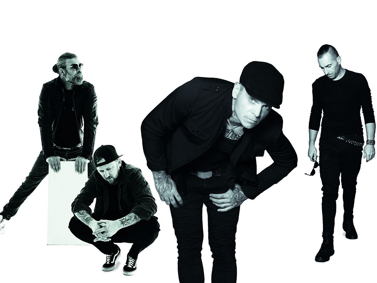 Die vier Bandmitglieder stehen in einem Dreieck, einer hockt. Alle tragen schwarze Kleidung und stehen vor einem weißen Hintergrund. 