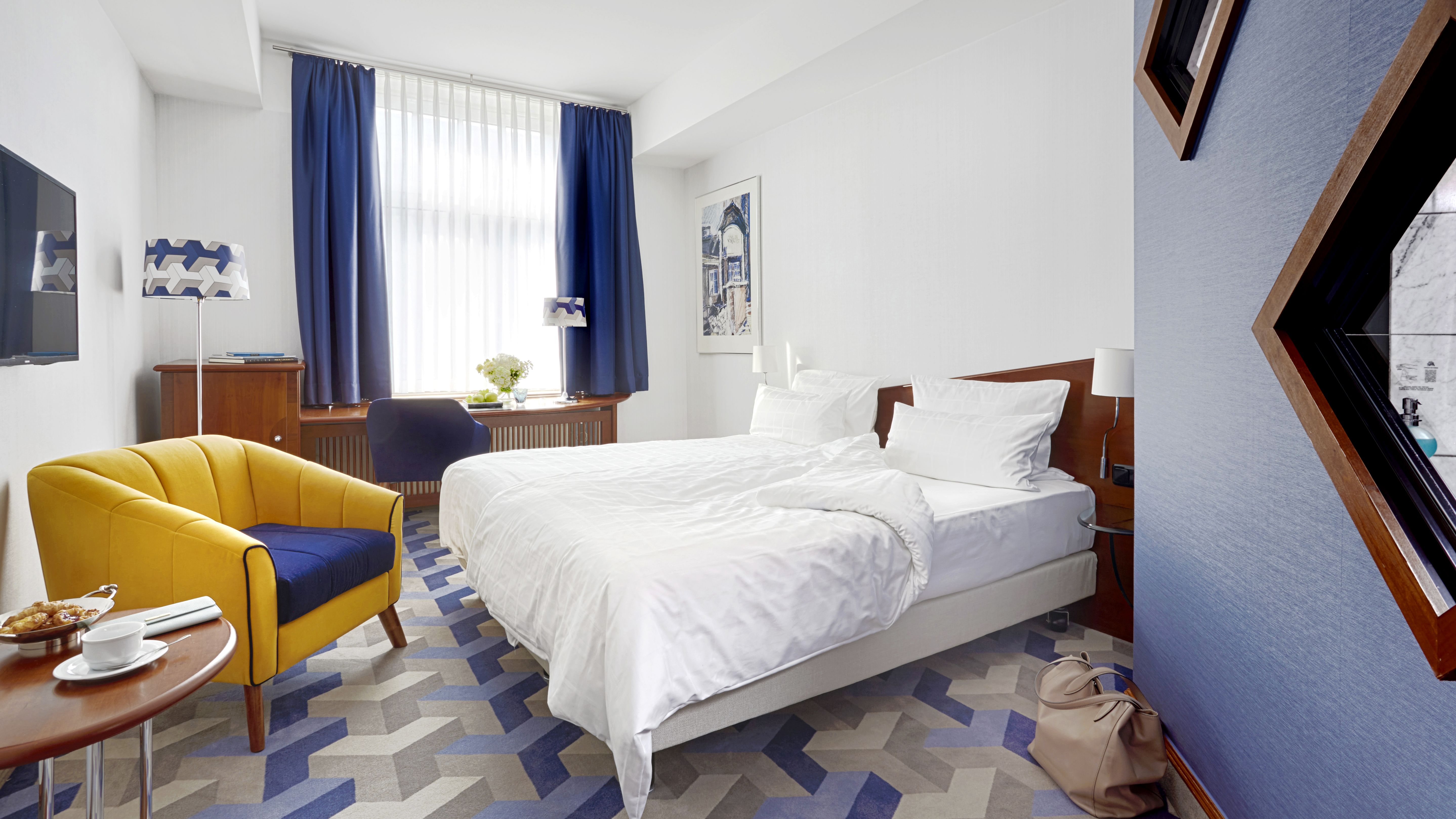 Modernes Hotelzimmer mit Doppelbett, Fenster, Sessel und TV.