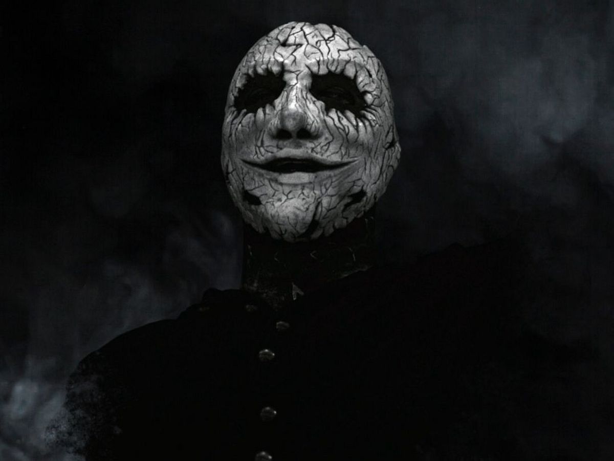 Ein Bild in schwarz-weiß mit einem Bandmitglied, der eine weiß-schwarze Maske trägt. 