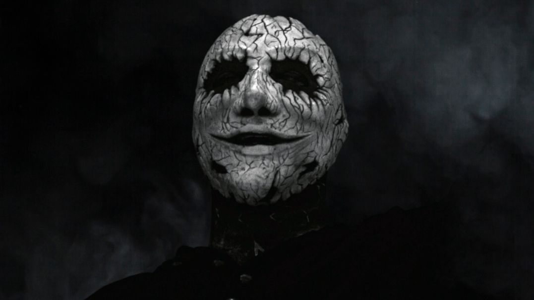 Ein Bild in schwarz-weiß mit einem Bandmitglied, der eine weiß-schwarze Maske trägt. 