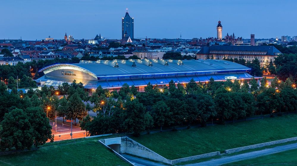 Blick auf die QUARTERBACK Immobilien ARENA am Abend vor der Skyline von Leipzig.