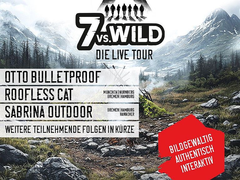 Im Vordergrund ist eine Feuerstelle mit einer selbstgebauten Holthütte zu sehen. Im Hintergrund sind Berge, die schneebedeckt sind. 