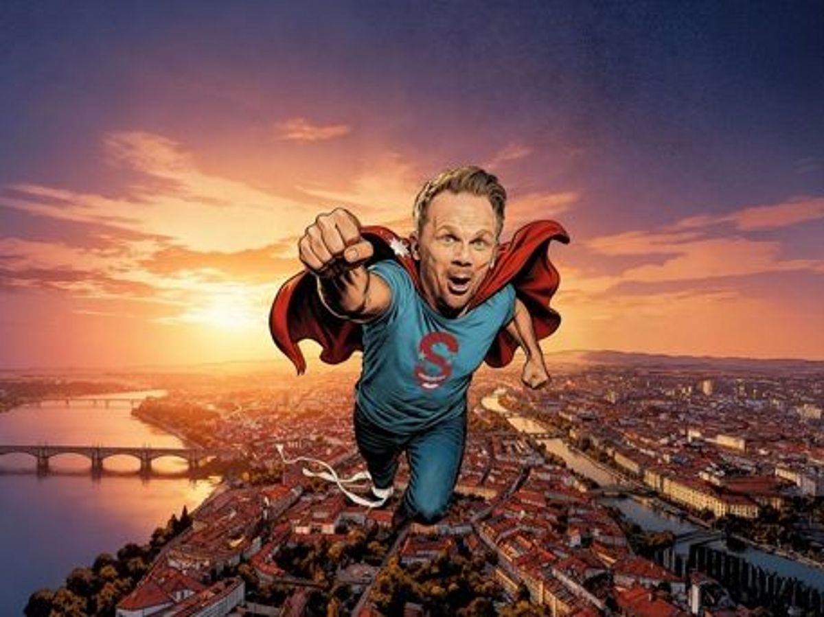Ralf Schmitz fliegt als Superman über eine  Großstadt bei Sonnenuntergang. Es hat comichafte Züge. 
