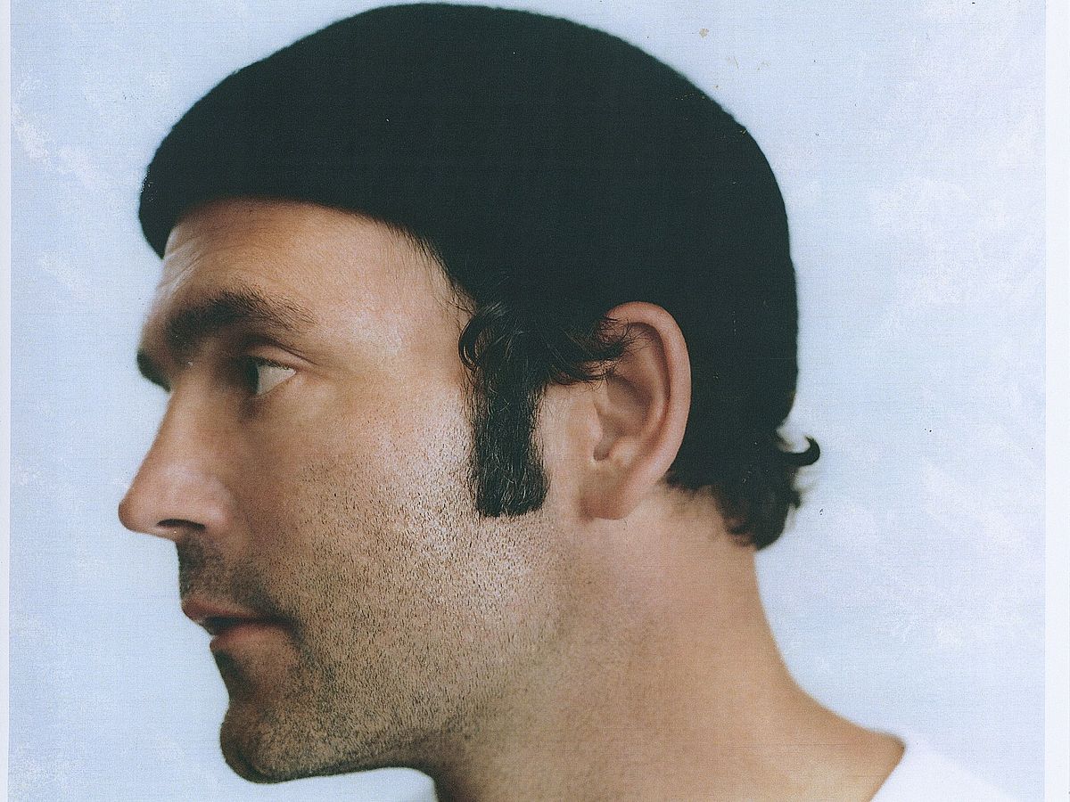 Ein Polaroidfoto von Bosse, der ein schwarzes Käppi und ein schwarzes T-Shirt trägt. Er steht vor einem weißen Hintergrund und schaut nach links. 