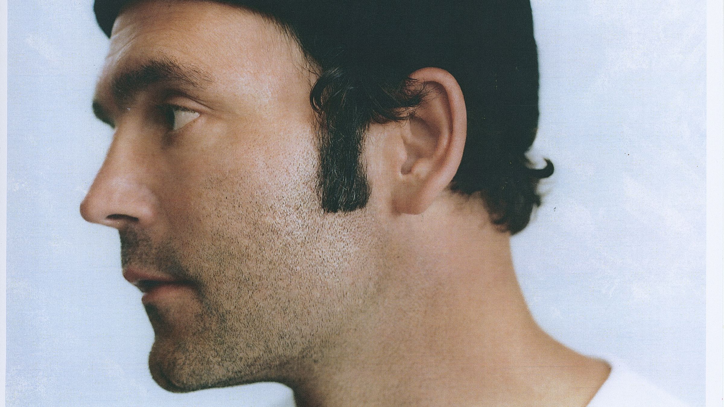 Ein Polaroidfoto von Bosse, der ein schwarzes Käppi und ein schwarzes T-Shirt trägt. Er steht vor einem weißen Hintergrund und schaut nach links. 