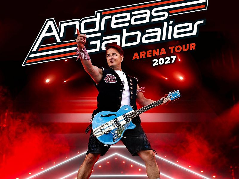 onzertplakat für Andreas Gabalier und seine „Arena Tour 2027“. In der Bildmitte steht der Musiker mit einer blauen E-Gitarre, die er um den Körper trägt. Er hebt einen Arm nach oben und zeigt mit dem Zeigefinger in die Luft. Er trägt ein weißes T-Shirt, eine schwarze Weste mit auffälligen Aufnähern und eine schwarze kurze Hose. Im Hintergrund sorgen intensive rote Scheinwerfer, Rauch und Lichteffekte für eine kraftvolle Konzertatmosphäre. Oben steht in großen, stilisierten weißen Buchstaben der Name „Andreas Gabalier“. Darunter sind in Rot „Arena Tour“ und in Weiß die Jahreszahl „2027“ zu lesen.