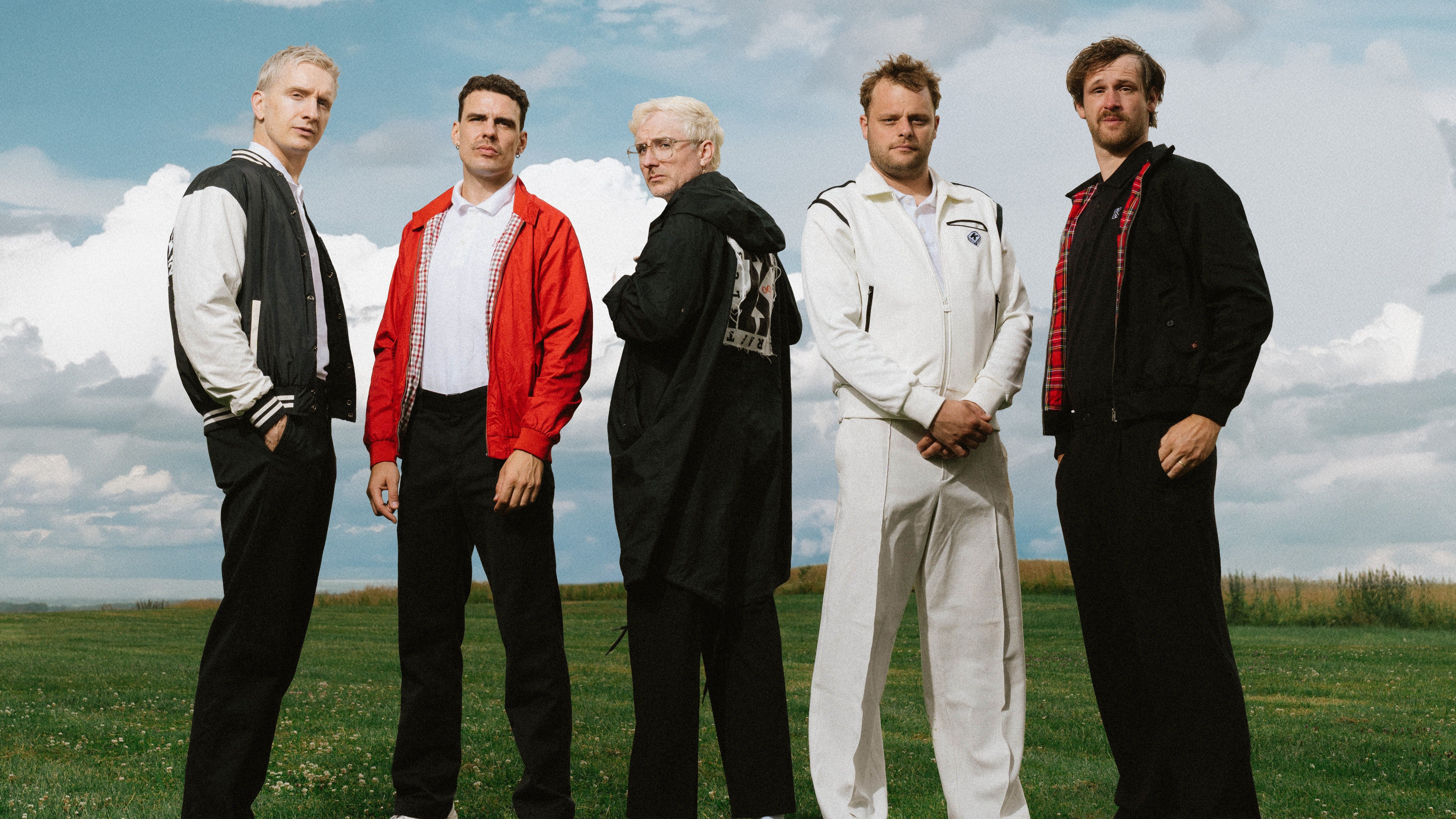 Die Band steht nebeneinander auf einer stilisierten grünen Wiese mit blauen, wolkigen Himmel. Sie alle tragen unterschiedliche Jacken. 