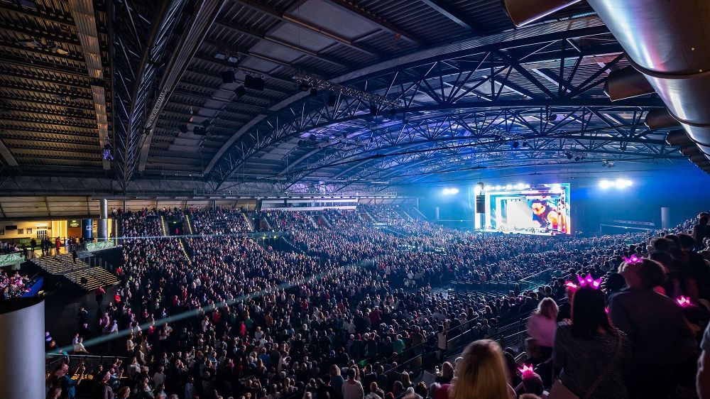 Der Innenraum der QUARTERBACK Immobilien ARENA ist voll mit Besuchern und eine Bühne im Hintergrund wird beleuchtet..