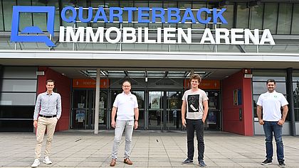 Vier Personen stehen vor der QUARTERBACK Immobilien ARENA. 