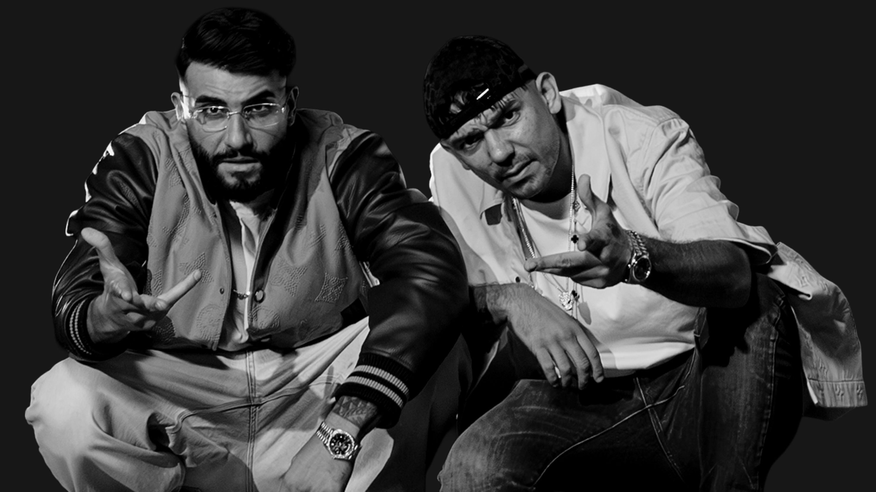 Ein schwarz-weißes Pressebild der beiden Rapper. Sie sind in der hocken und halten jeweils mit einer Geste eine Hand nach vorne. 