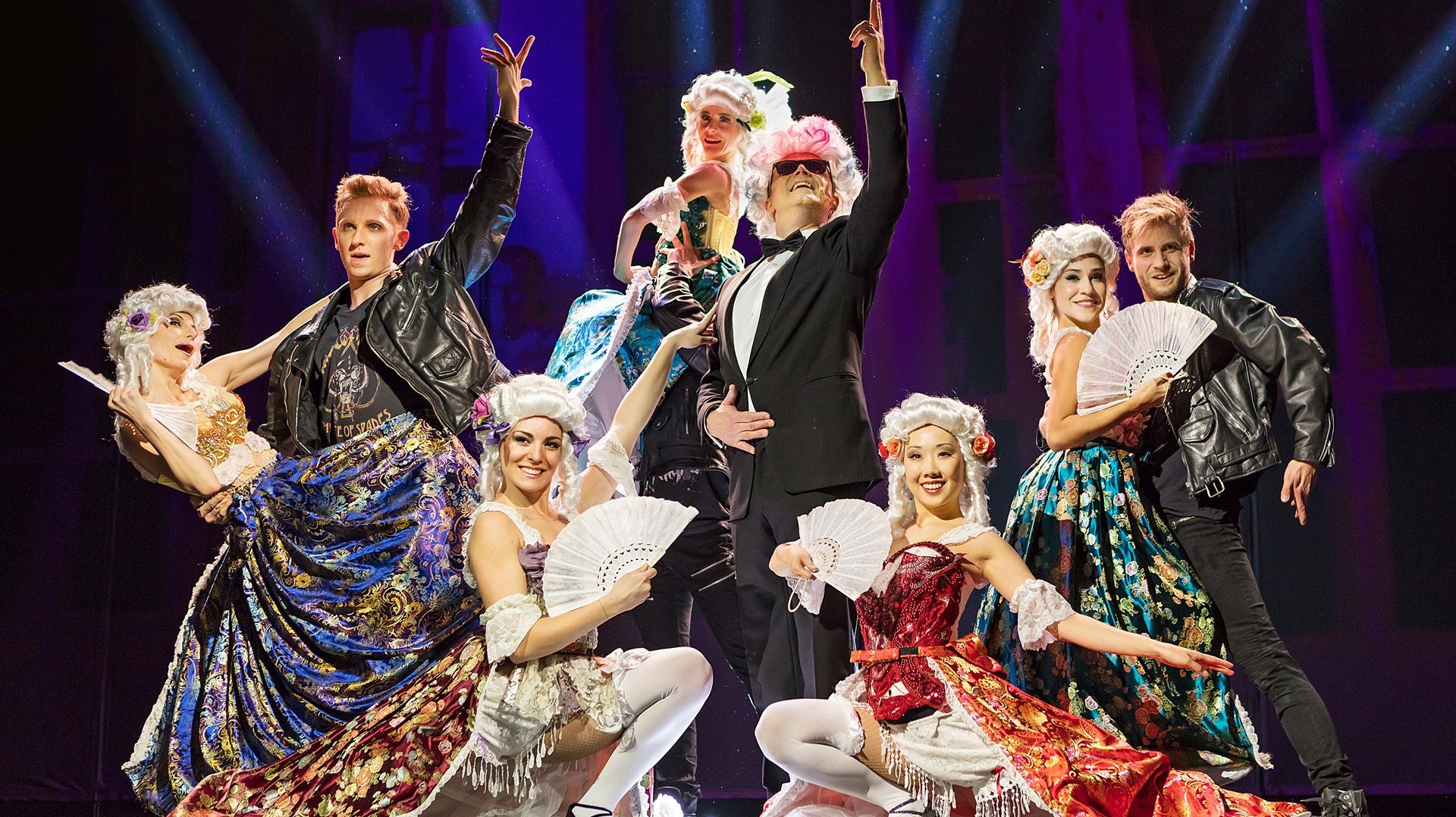 Der Falco-Darsteller steht mit einer Tanzcrew auf der Bühne. Die Frauen und Falco tragen eine Perücke, die Frauen tragen Kleider aus der Zeit Mozarts. Die Männer tragen Lederjacken, nur Falco trägt einen schwarzen Anzug. 