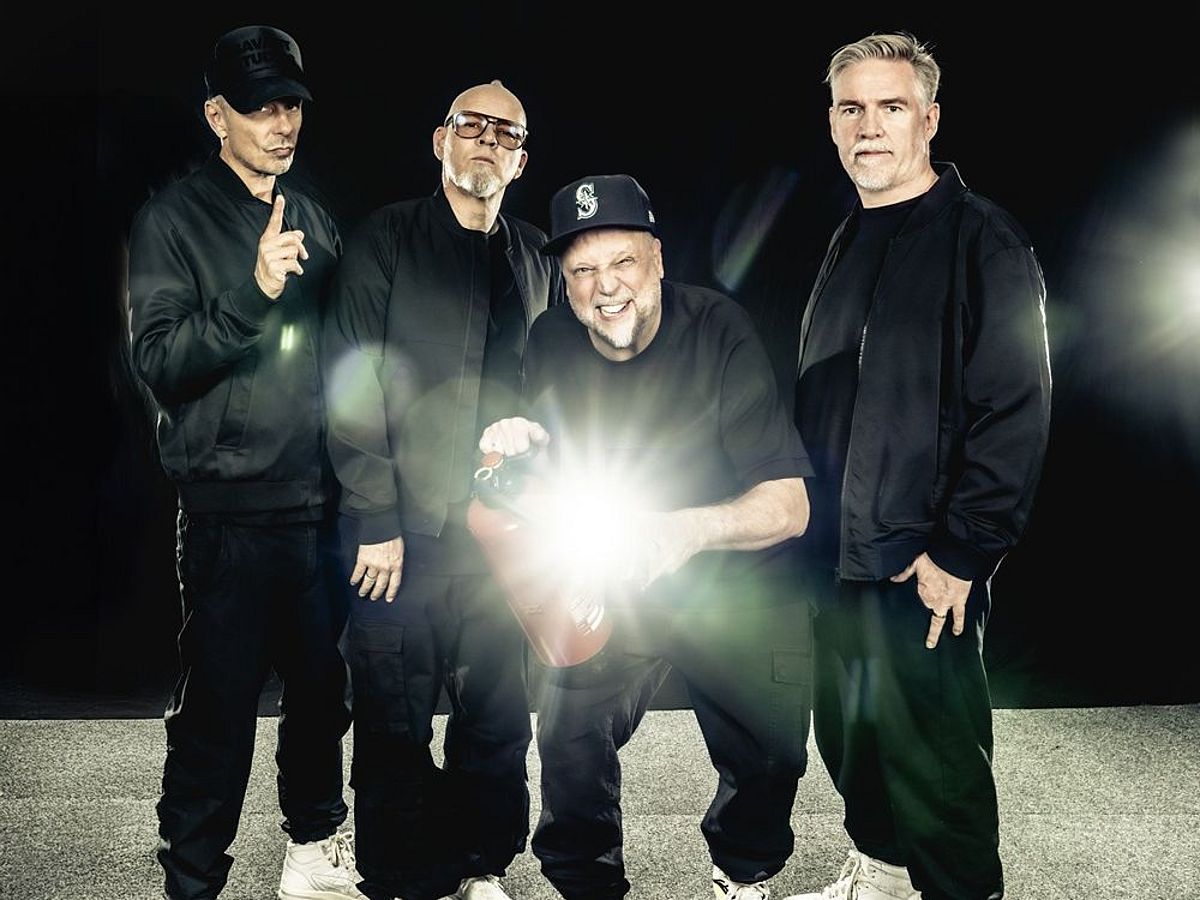 Die Band steht in dunkler Kleidung vor einem dunklen Hintergrund. Smudo hat einen Feuerlöscher in der Hand und verzieht sein Gesicht. Entweder macht er ein Selfie oder der Feuerlöscher reflektiert stark, da ein heller Lichtfleck vor Smudos Körper zu sehen ist. 