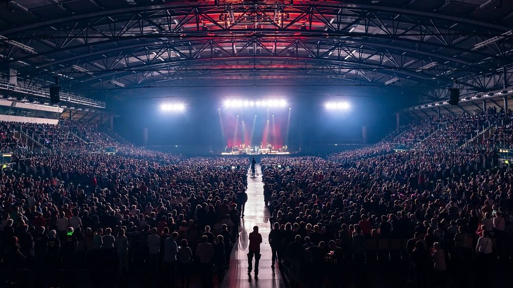 Eine Bühne in der QUARTERBACK Immobilien ARENA wird erleuchtet und davor befinden sich zahlreiche Leute.