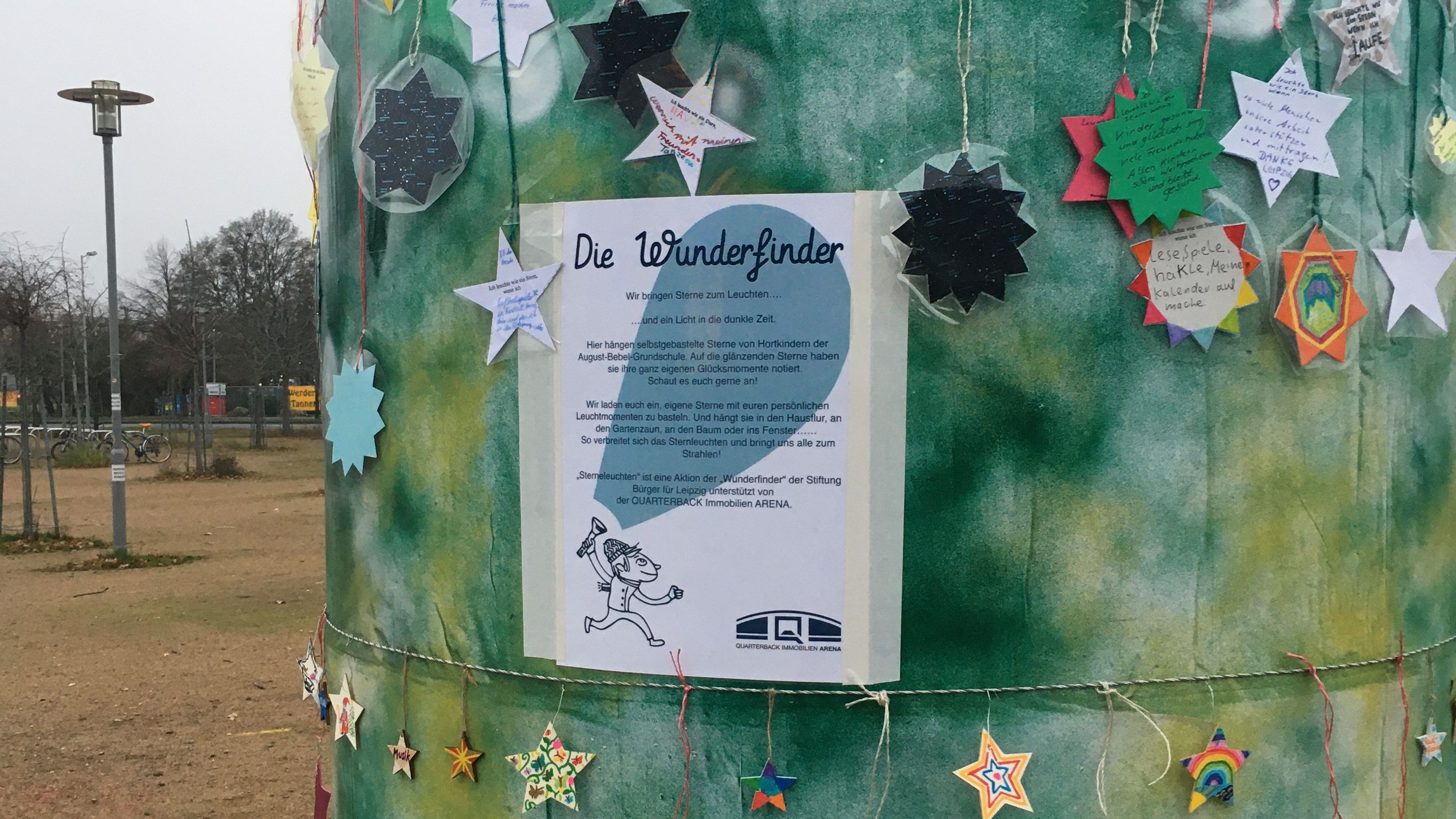 Ein Ausschnitt einer grün besprühten Litfaßsäule mit vielen Sternen an Bändern. 