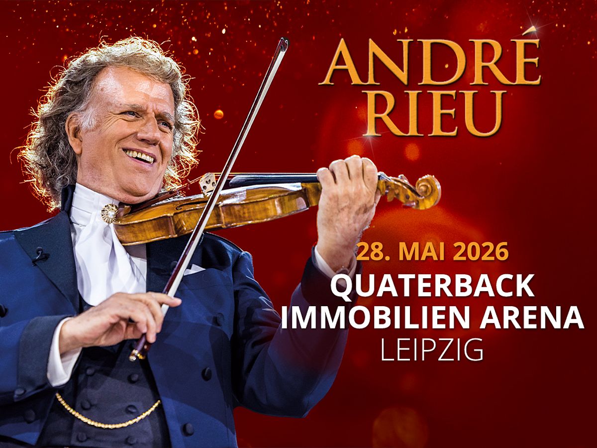 André Rieu trägt einen blauen Anzug mit einem weißen Hemd. Er hält eine Geige. 