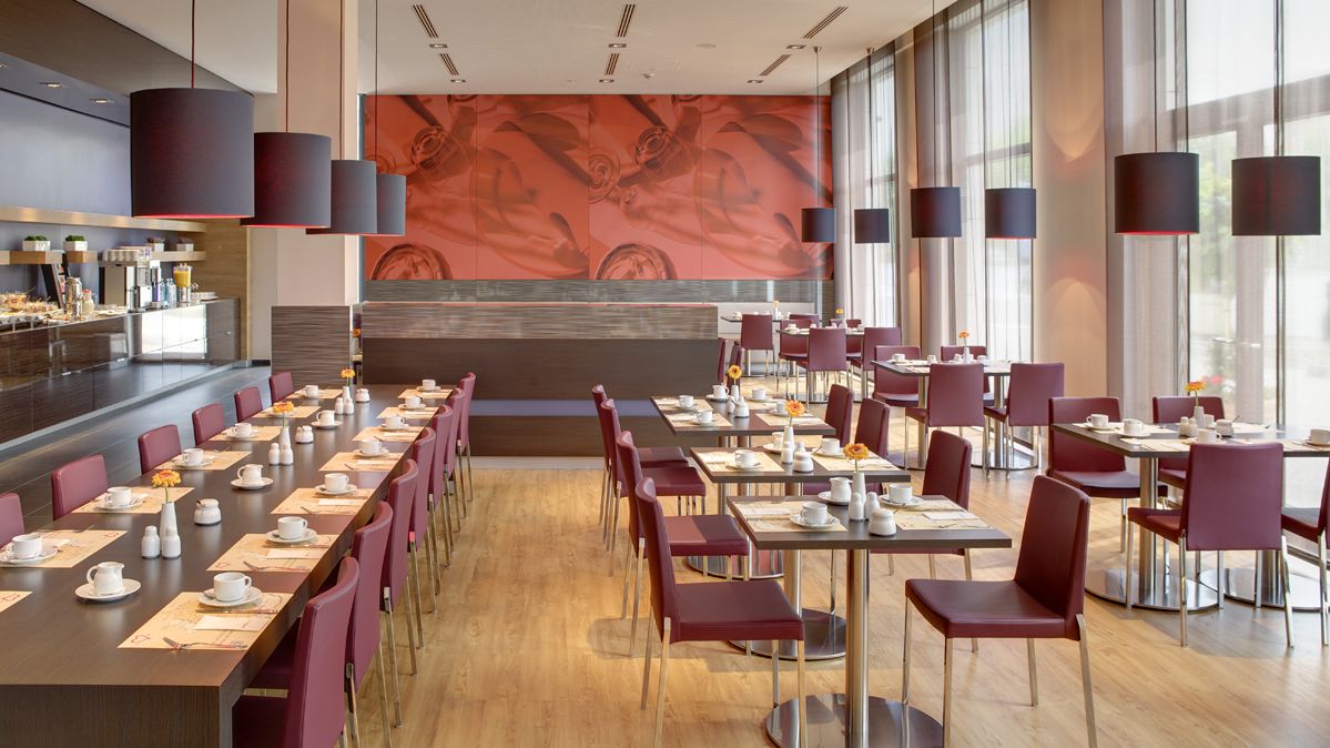 Sicht auf den Frühstücksraum des Hotels mit gedeckten Tischen. Es sind mehrere kleine Tische sowie eine lange Tafel zu sehen. 