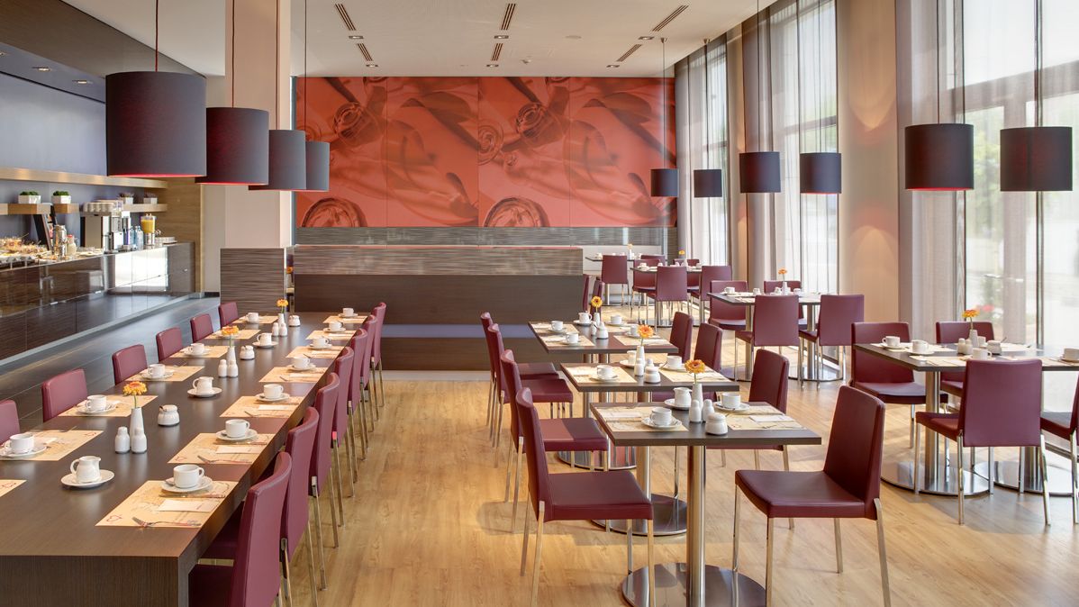 Sicht auf den Frühstücksraum des Hotels mit gedeckten Tischen. Es sind mehrere kleine Tische sowie eine lange Tafel zu sehen. 