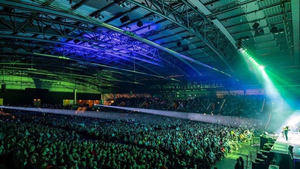 Blick schräg von der Bühne in einen grün blau beleuchteten Innenraum einer vollen QUARTERBACK Immobilien ARENA.