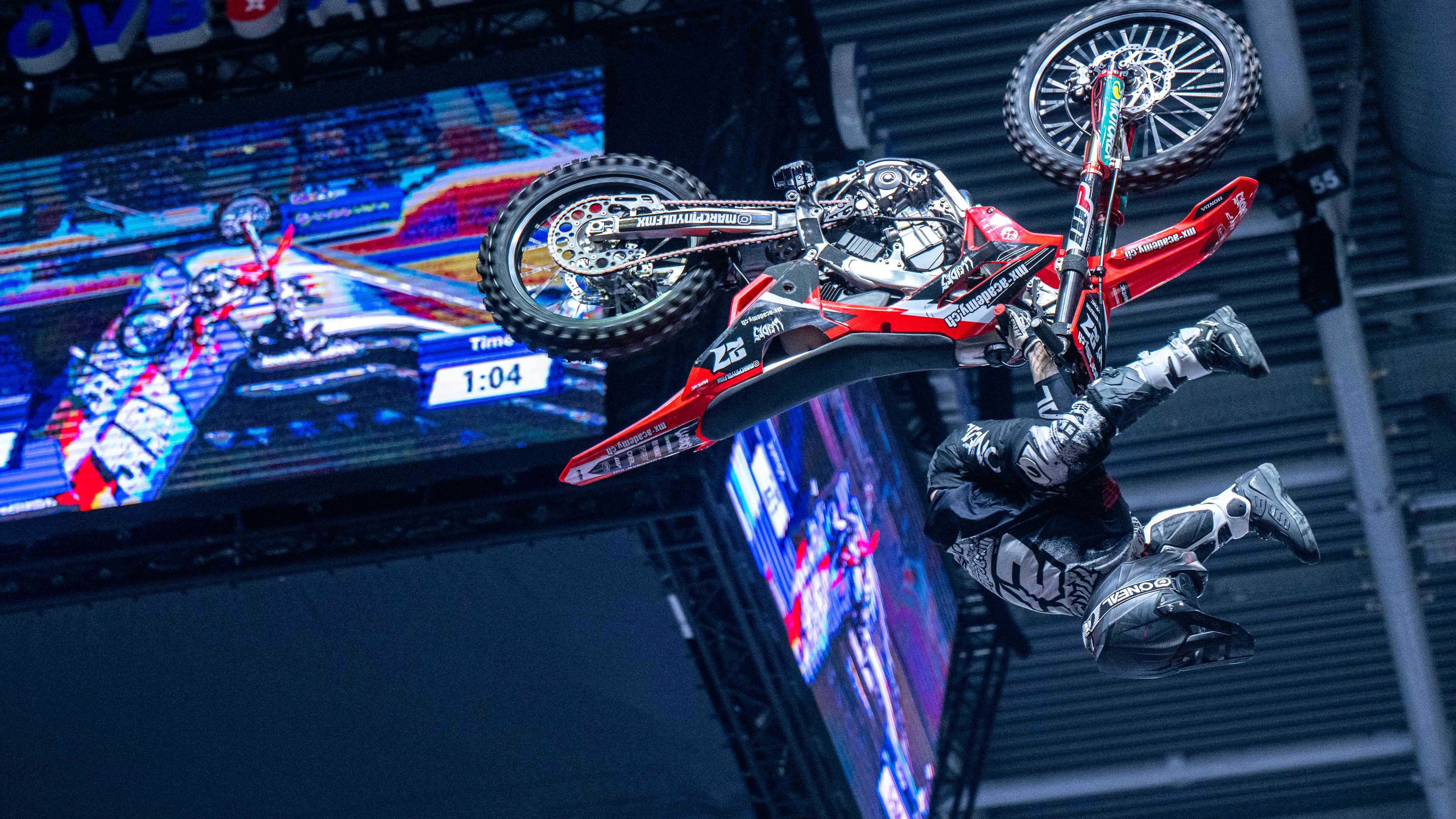 Ein Motorradfahrer macht in einer Halle ein Salto. Der Fahrer ist gerade auf dem Kopf. 