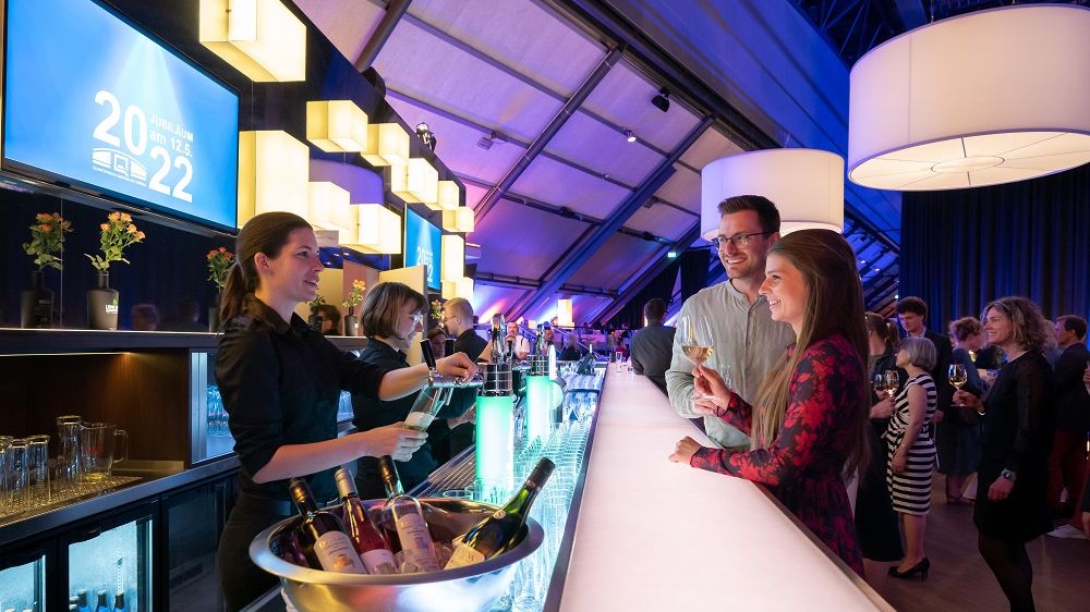 An einer Bar wird ein Pärchen von einer Barkeeperin bedient, die gerade ein Bier zapft.