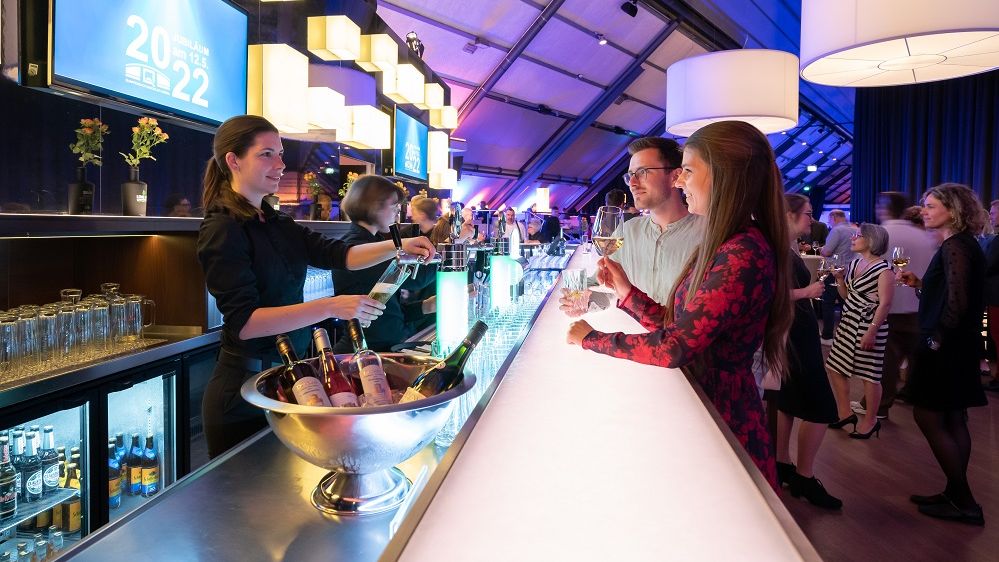 An einer Bar wird ein Pärchen von einer Barkeeperin bedient, die gerade ein Bier zapft.