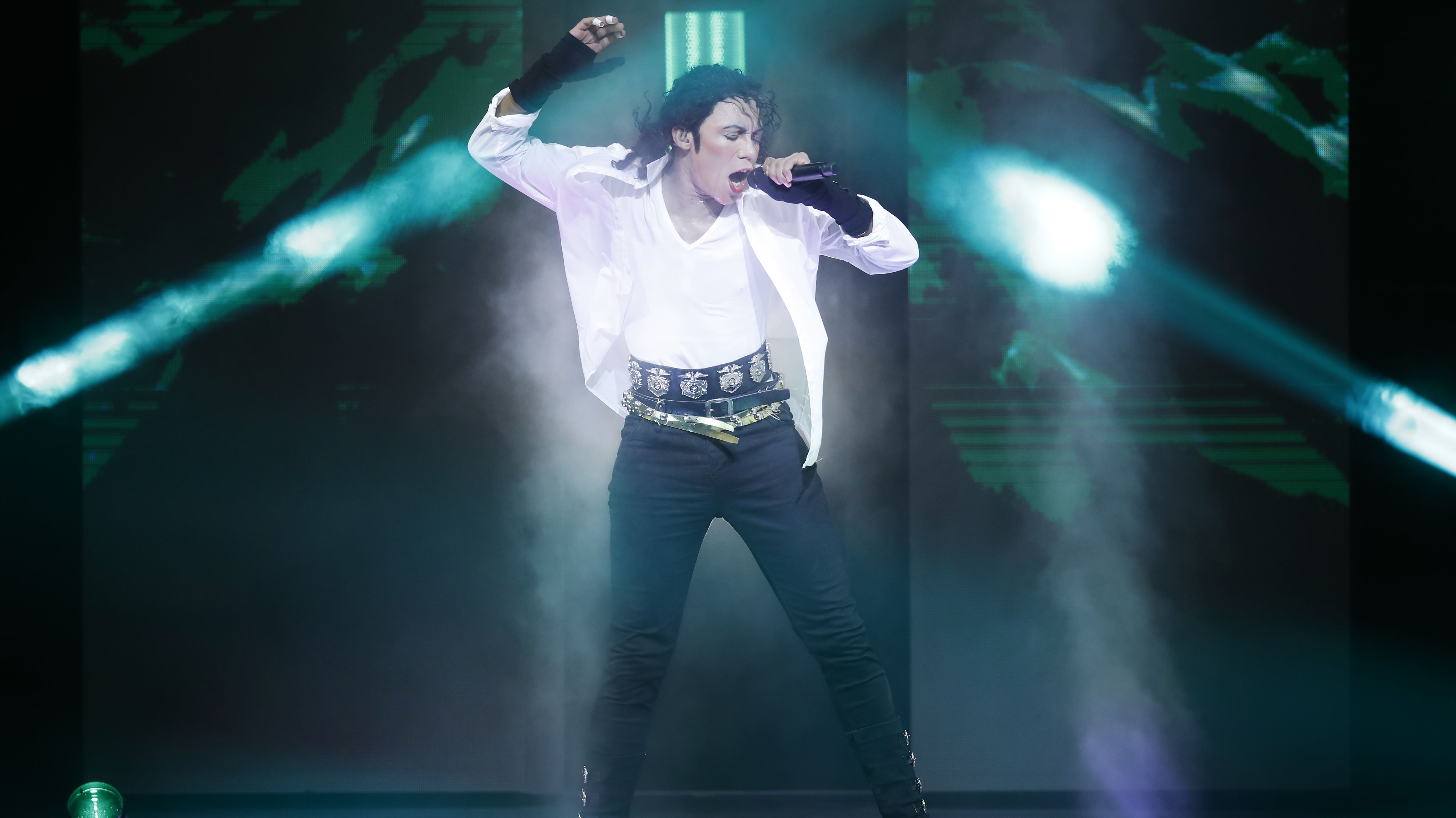 Ein Michael Jackson Darsteller im weißen Hemd hat ein Mikrofon in der Hand. 