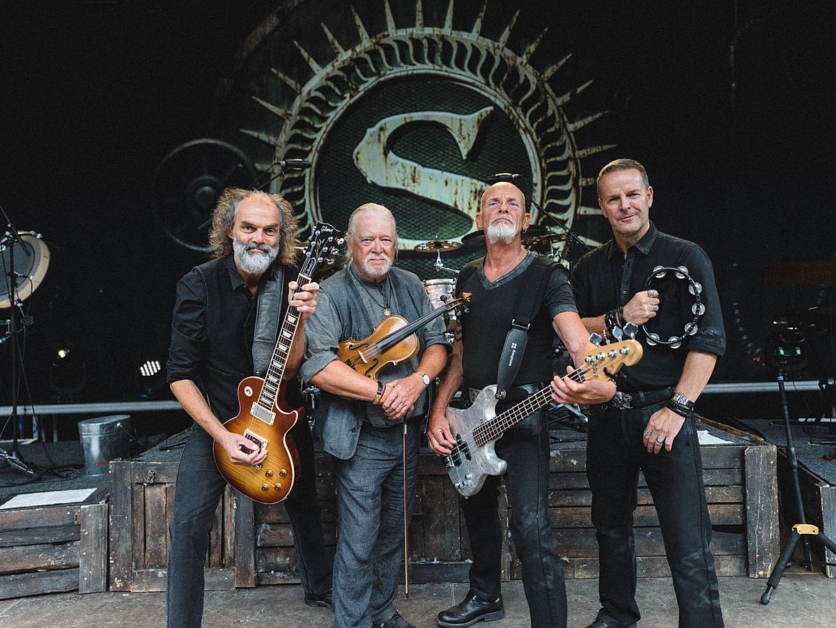 Die Band steht mit ihren Instrumenten auf der Bühne. Im Hintergrund ist ein großes S zu sehen. 