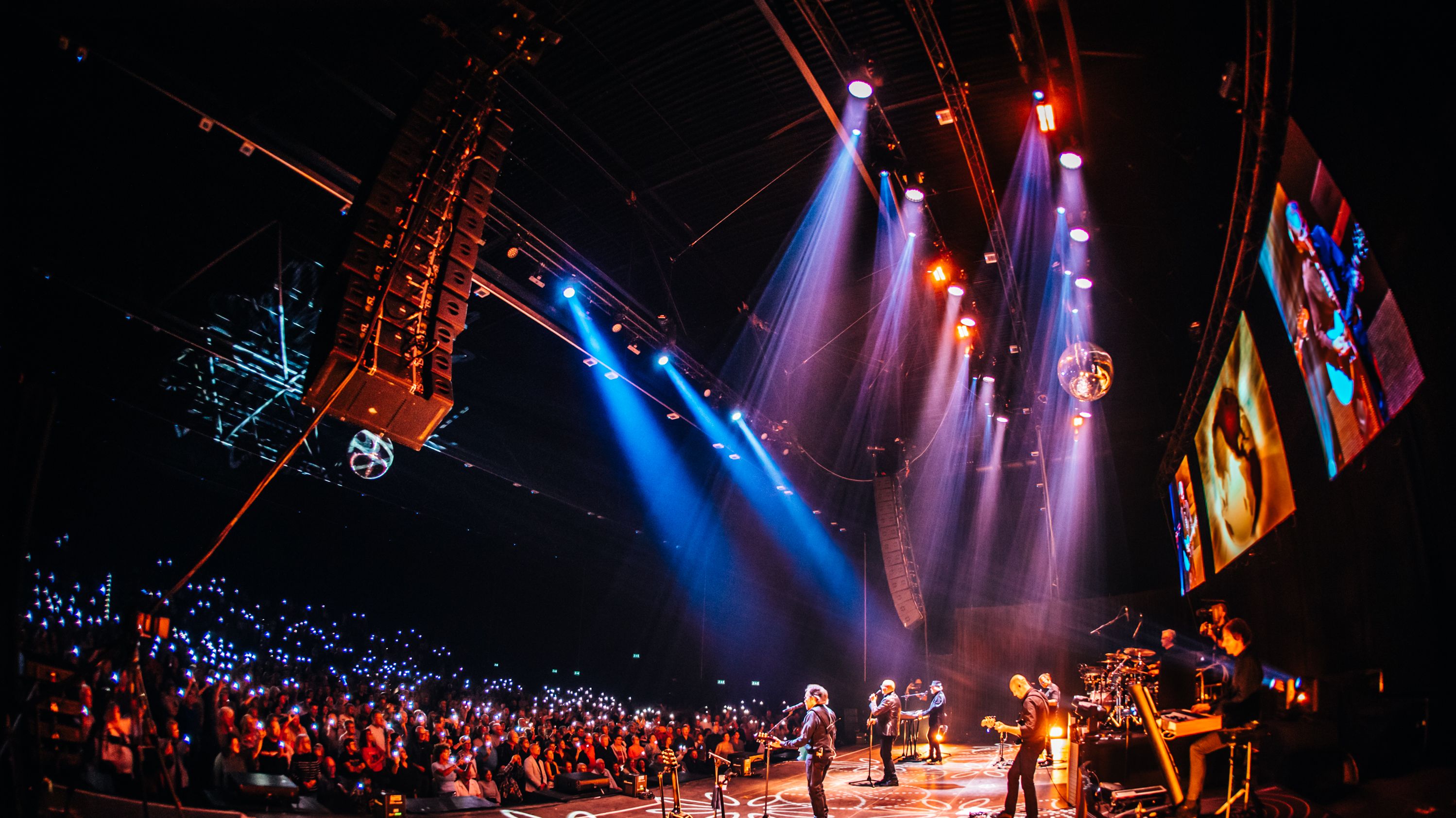 Die Band steht auf der Bühne, sie tragen weiße Anzüge. 