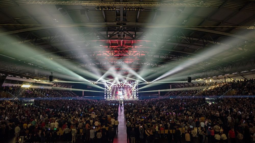 Der Innenraum der QUARTERBACK Immobilien ARENA wird von Strahlern erleuchtet und ist voll mit Besuchern.