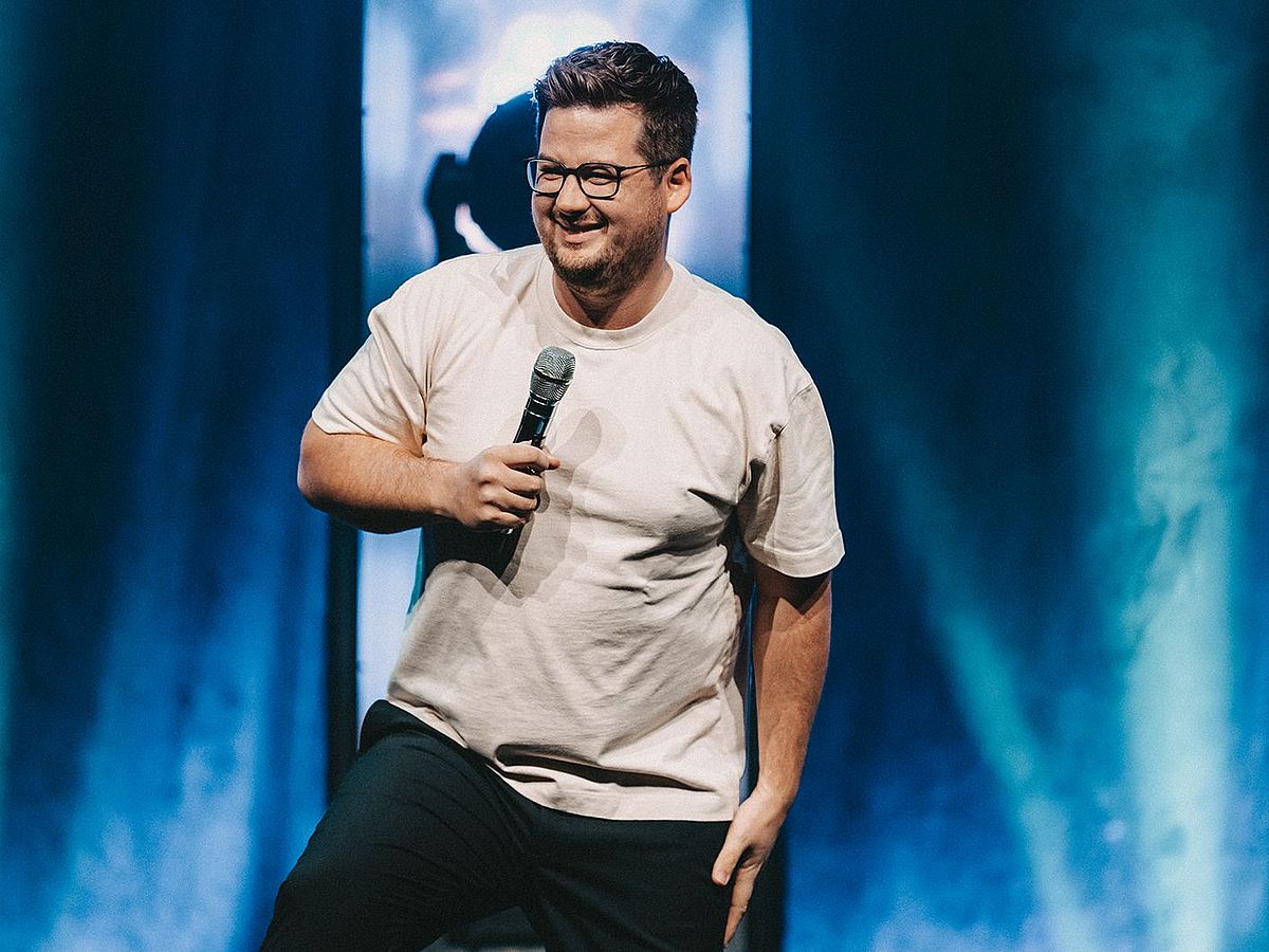 Chris Tall steht auf einer Bühne mit einem Mikrofon in der Hand. 