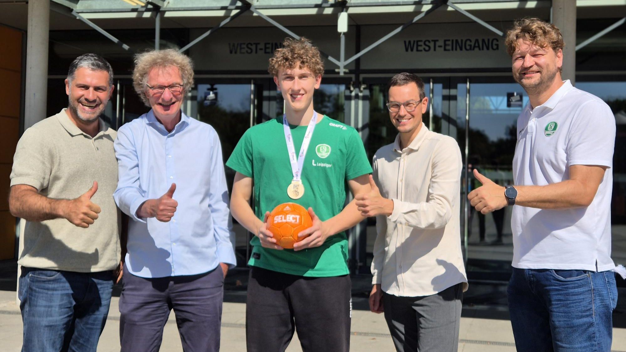 Karsten Günther (SC DHfK), Michael Kölmel (ZSL), Anton Voss (SC DHfK), Philipp Franke (ZSL) und Matthias Albrecht stehen vor der QUARTERBACK Immobilien ARENA. Anton Voss hat einen Handball in der Hand, alle anderen halten den Daumen hoch. 