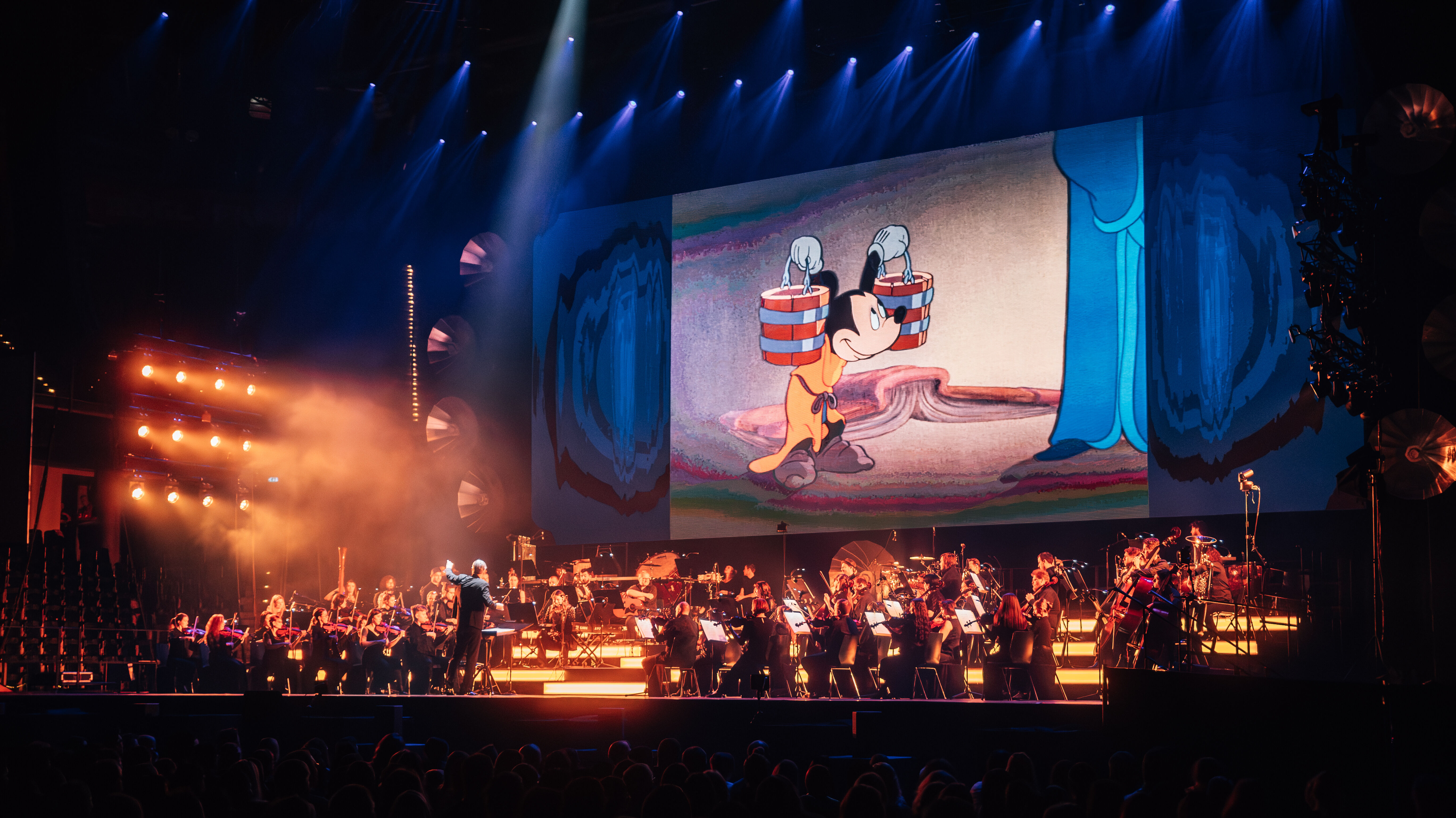 Ein Orchester ist auf der Bühne, im Hintergrund läuft ein Disney-Film.