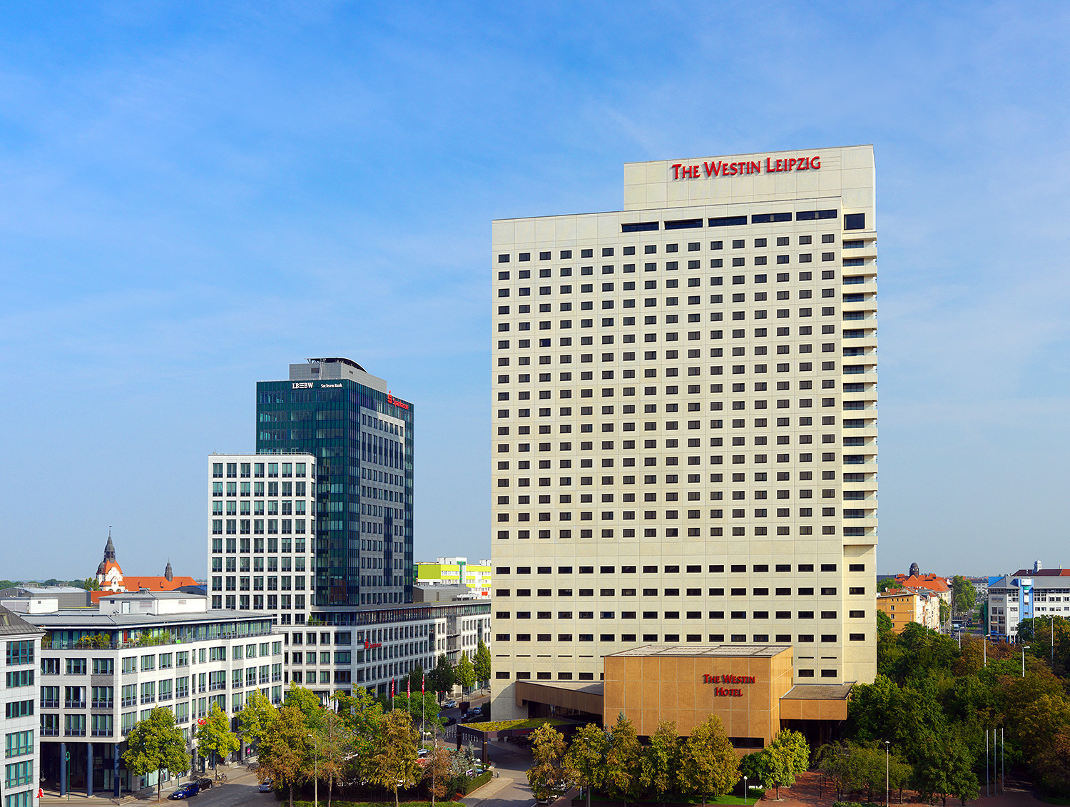 Ein hohes weißes Hotelgebäude steht in der Leipziger Innenstadt und auf dem Gebäude steht oben rechts The Westin Leipzig in roter Schrift.