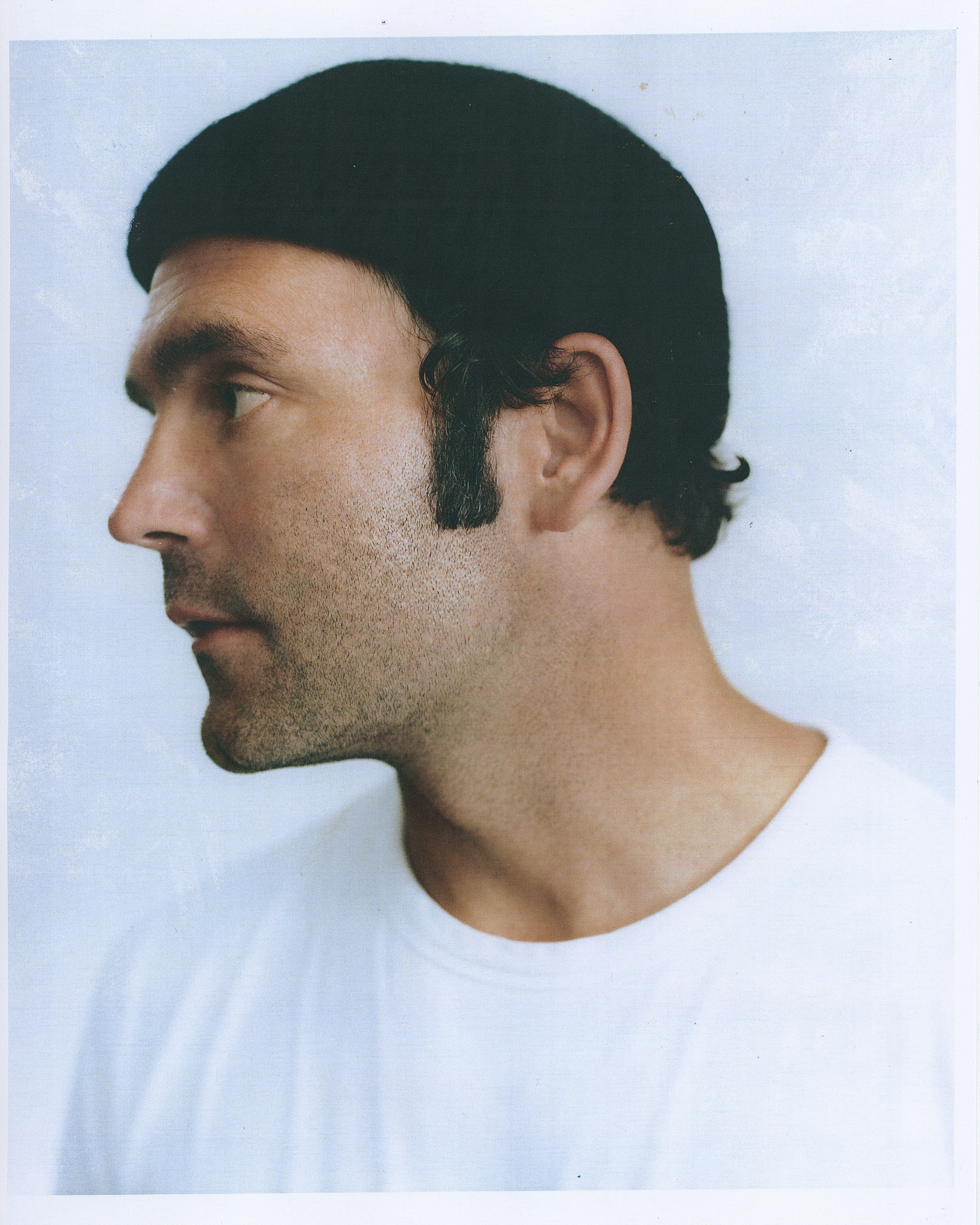 Ein Polaroidfoto von Bosse, der ein schwarzes Käppi und ein schwarzes T-Shirt trägt. Er steht vor einem weißen Hintergrund und schaut nach links. 