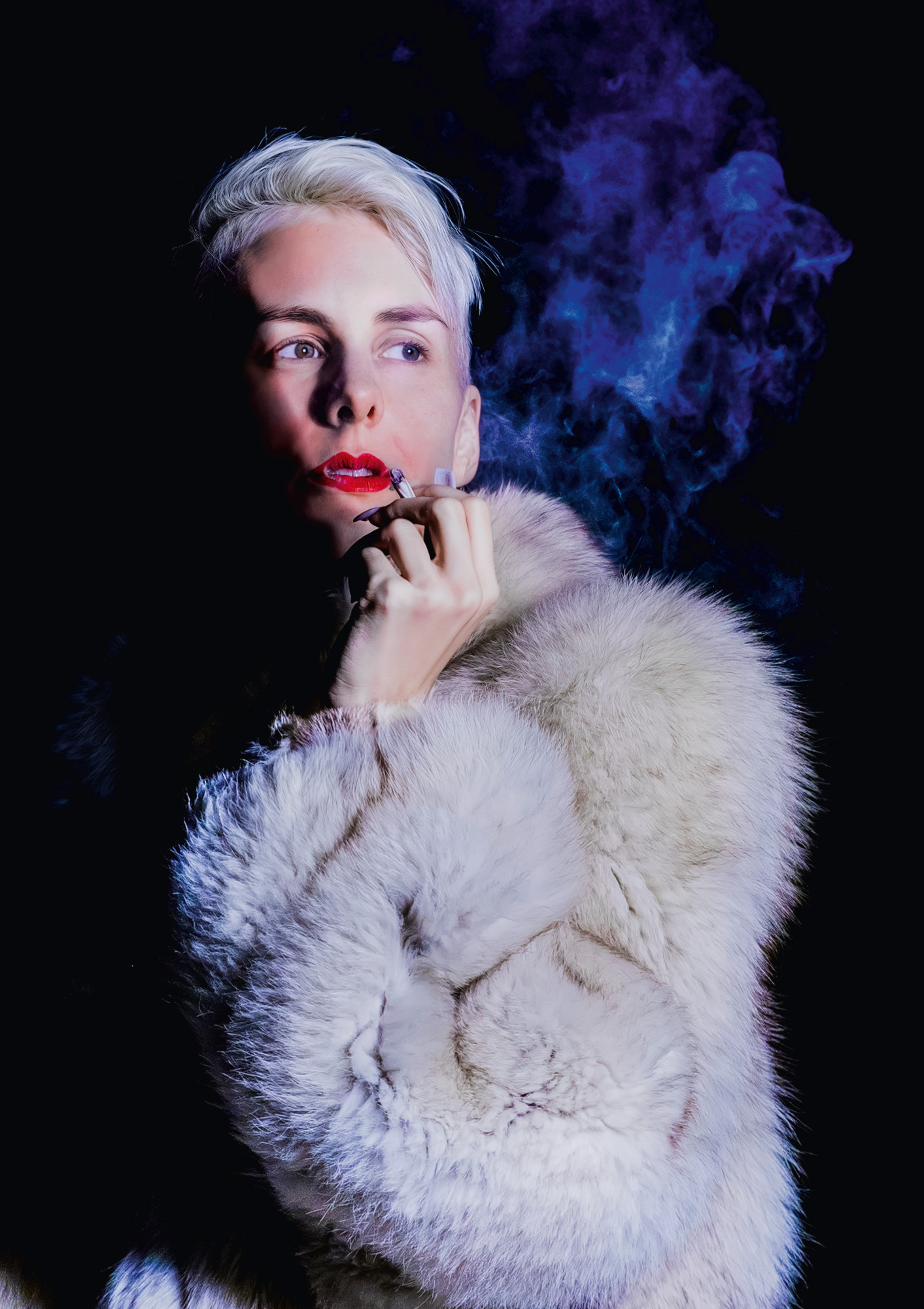Lisa Eckhart mit rotem Lippenstift trägt einen weißen Pelz und hält eine Zigarette in der Hand.